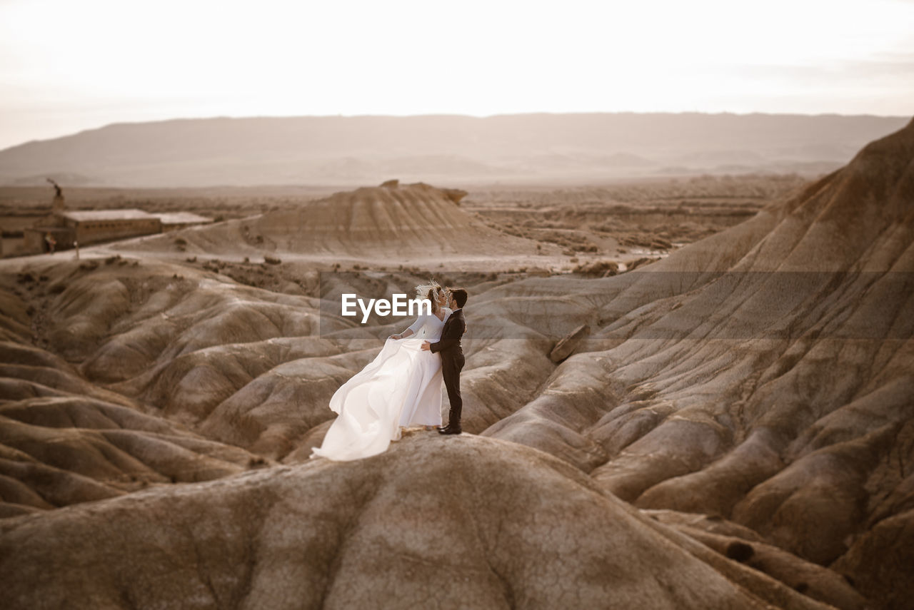 High angle of groom and bride embracing near mountain against cloudy sundown sky in bardenas reales natural park in navarra, spain