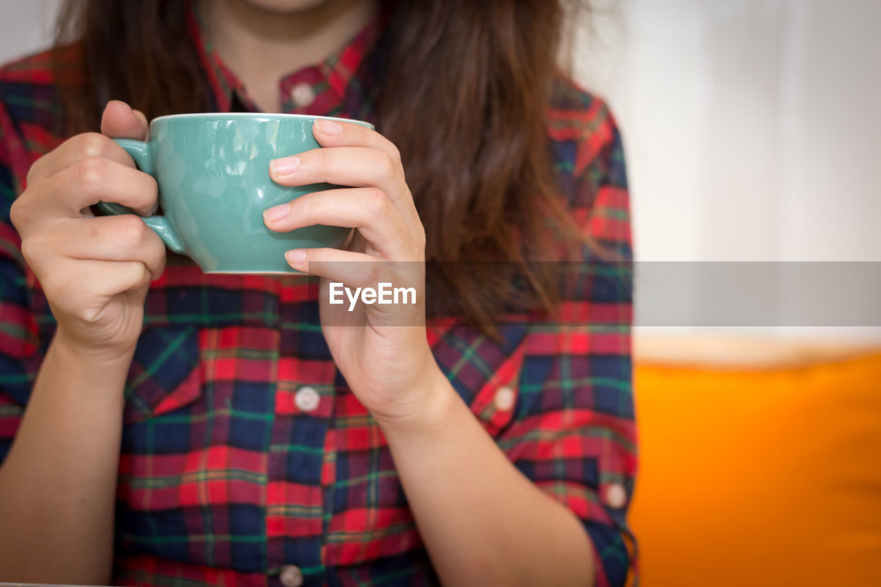 Midsection of woman holding coffee cup at home