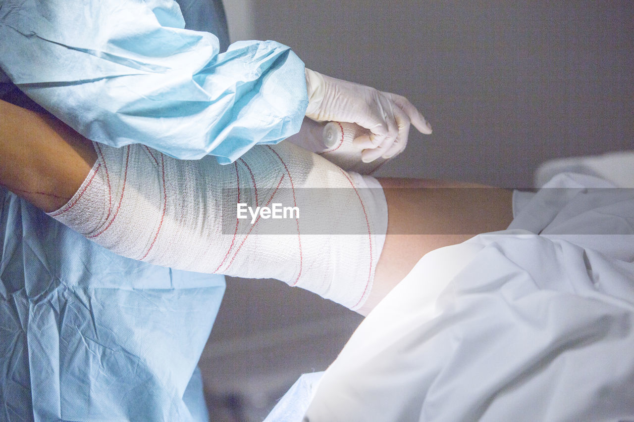 Midsection of doctor wrapping adhesive bandage on patient leg in hospital