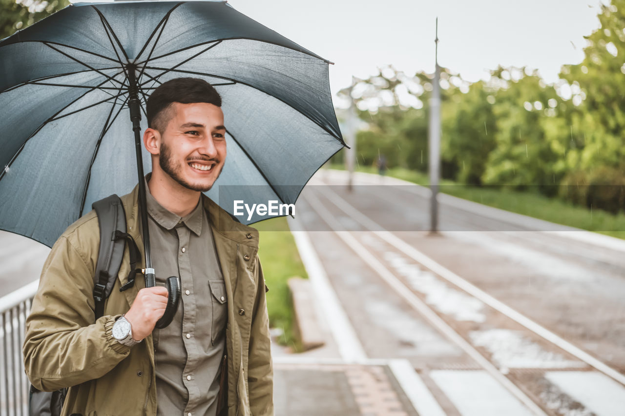 Man with umbrella  on a rainy day. handsome young tourist with backpack is crossing the road