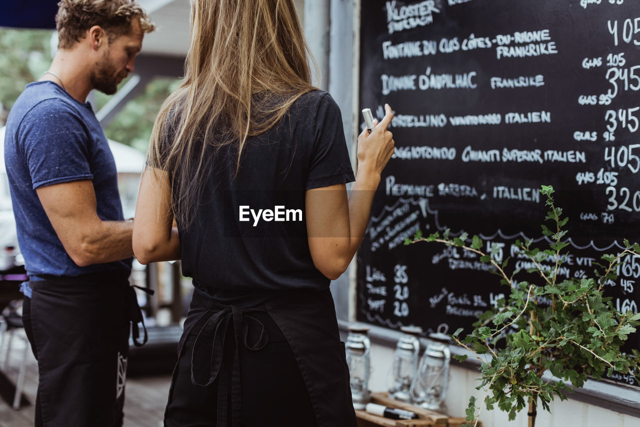 Rear view of businesswoman standing with coworker against wall in restaurant