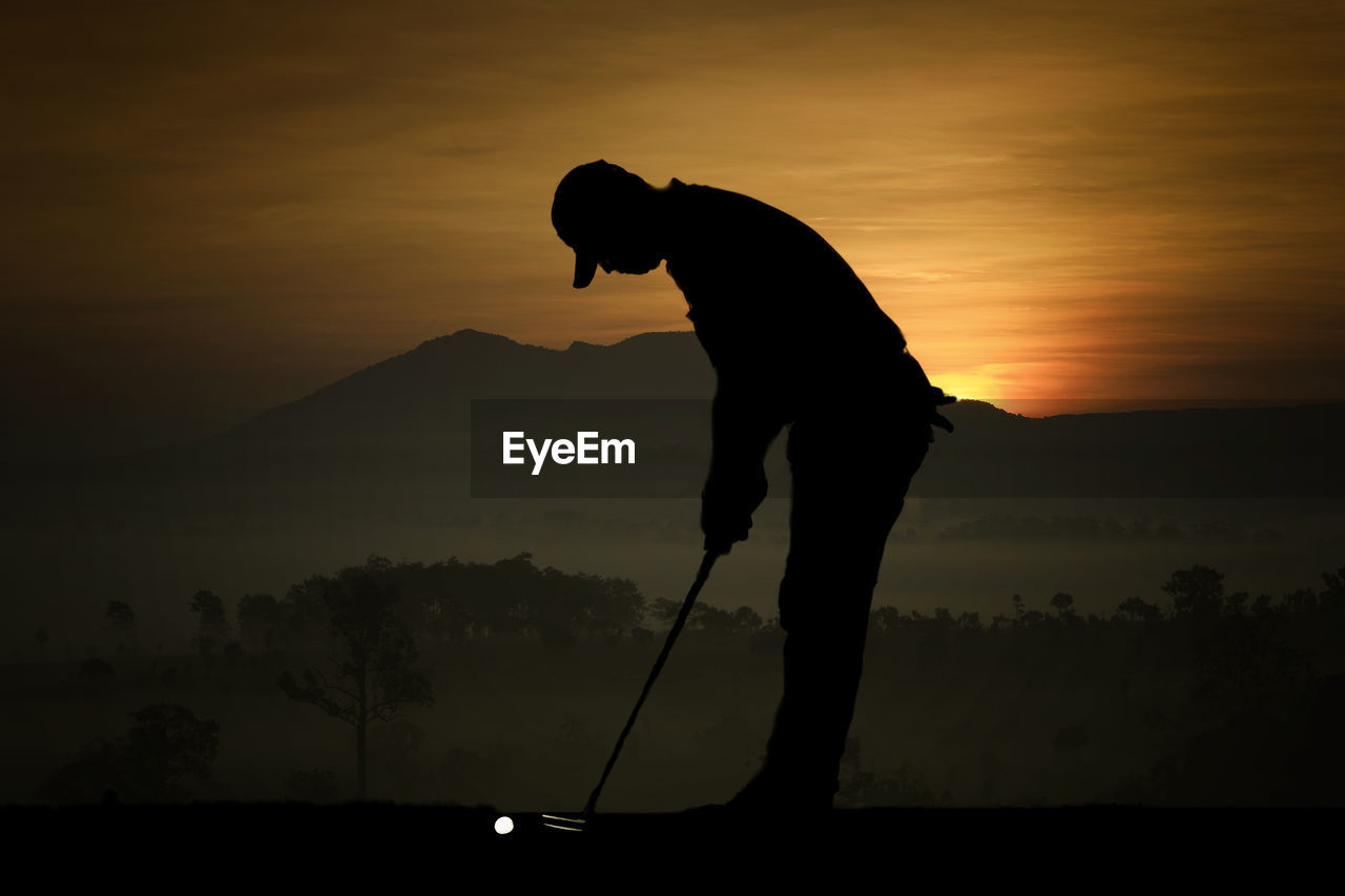 Silhouette man playing golf on field against sky during sunset