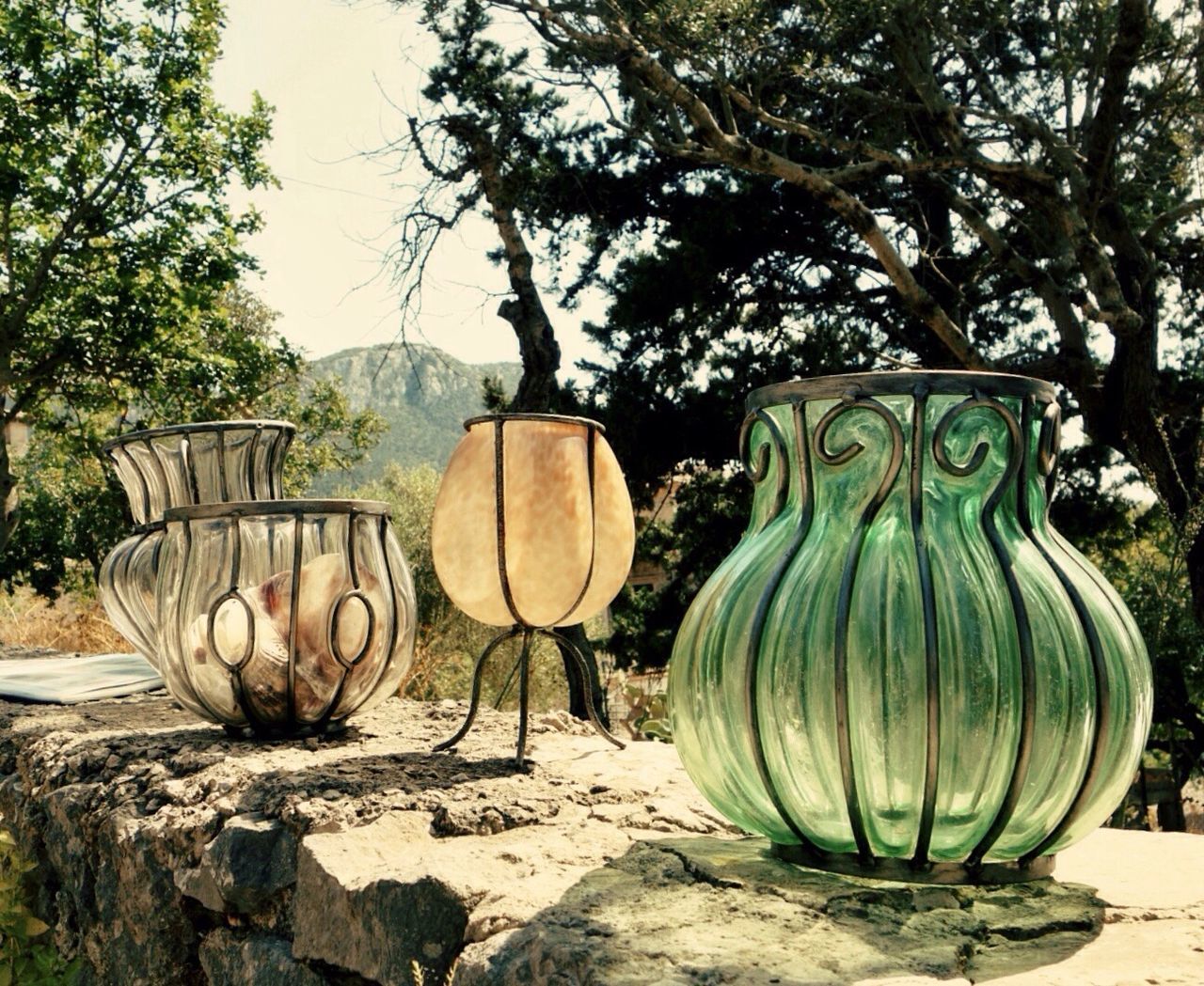Close-up of glass jars on stone wall against trees