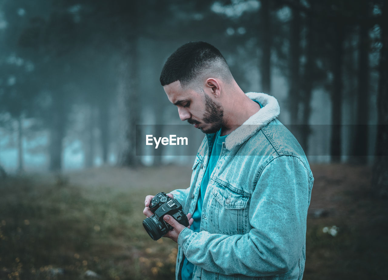 SIDE VIEW OF YOUNG MAN HOLDING CAMERA