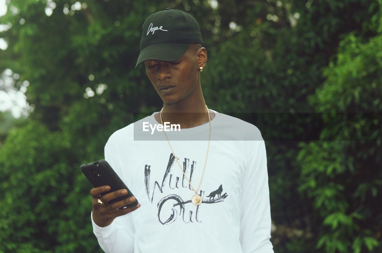 Man using smart phone against trees