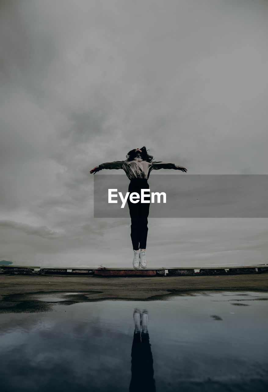 Full length of woman jumping by water against sky