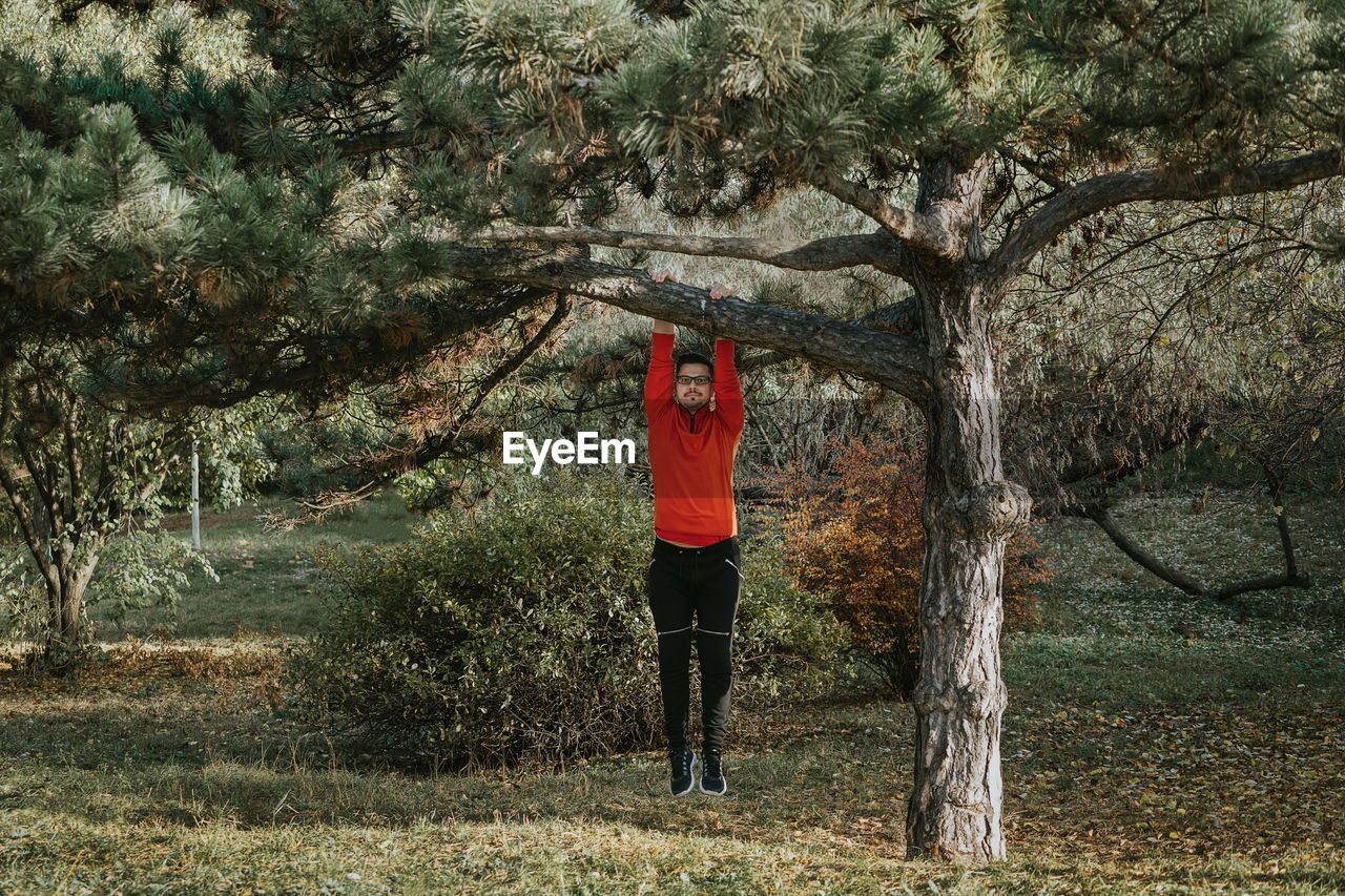 Full length of man hanging from branch in forest