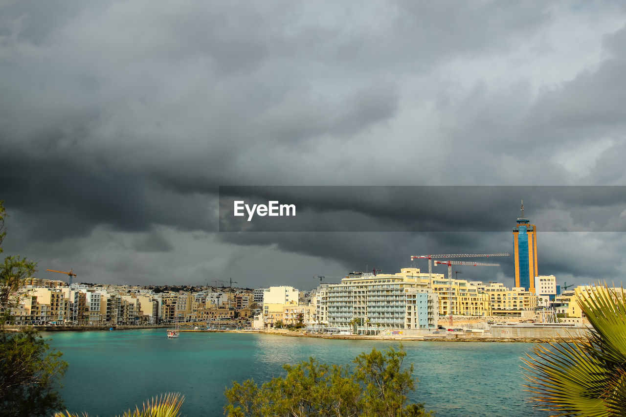 Sea by building against cloudy sky