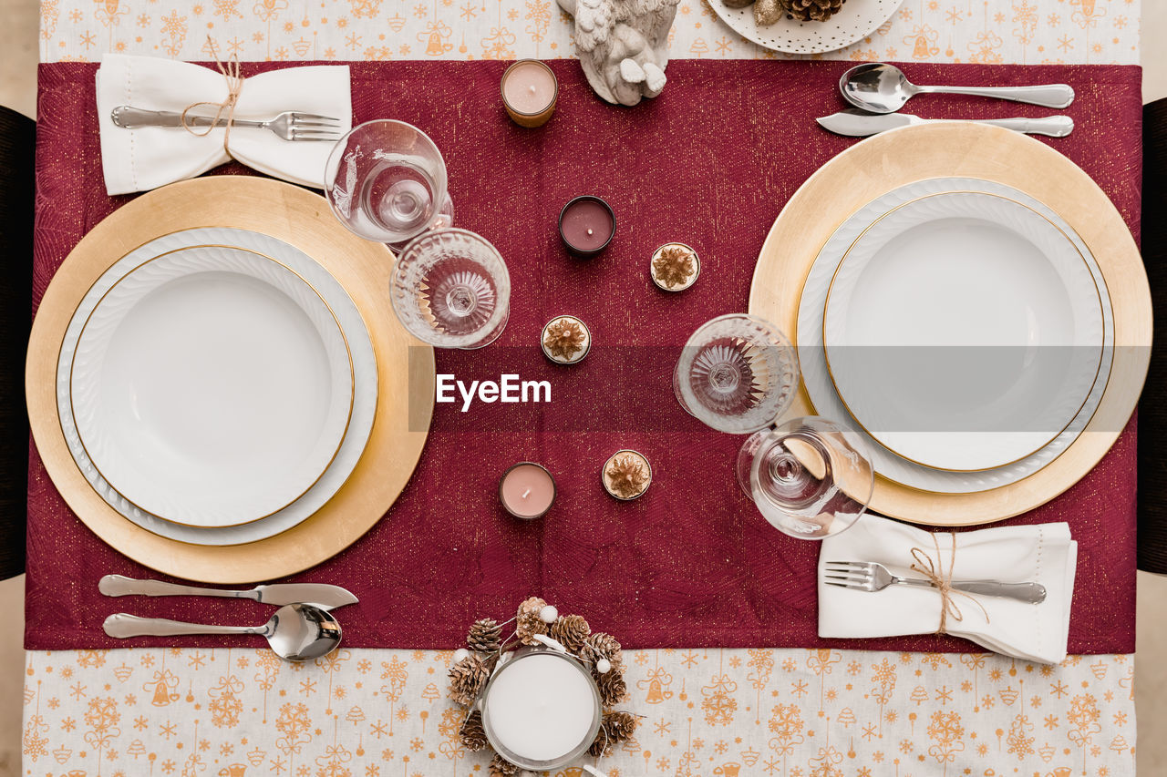 Top view of table setting with glasses and cutlery near plates decorated with candles and cones for christmas celebration