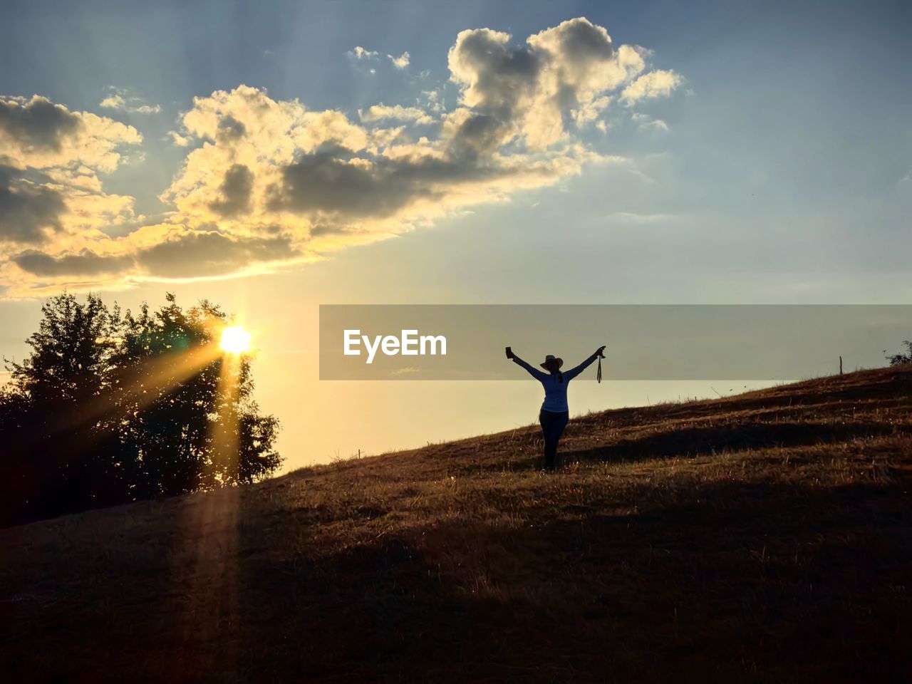 rear view of man with arms outstretched standing on field against sky during sunset