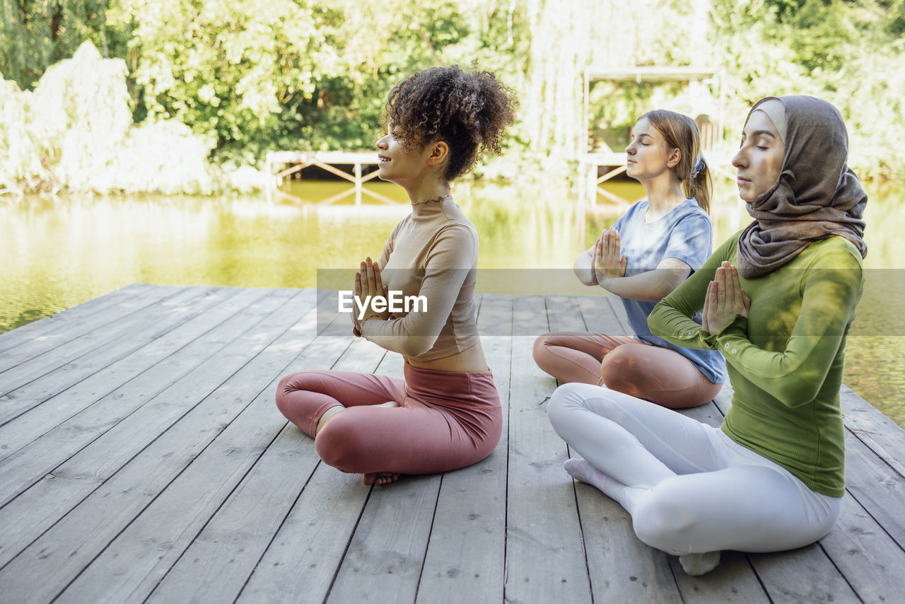 side view of mother and daughter sitting on pier over lake