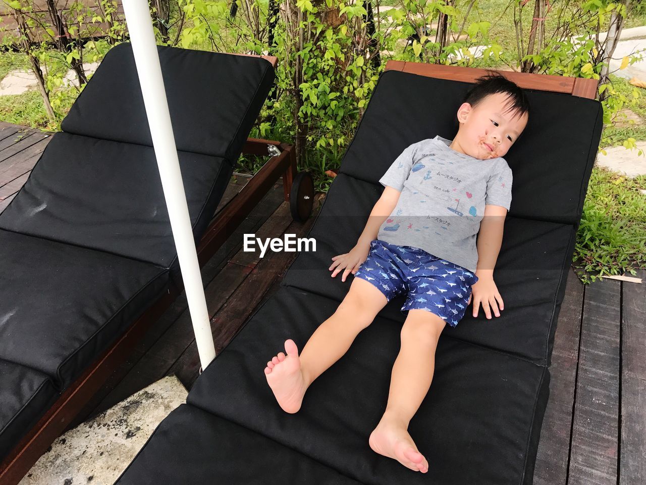 High angle view of cute boy lying on deck chair over boardwalk