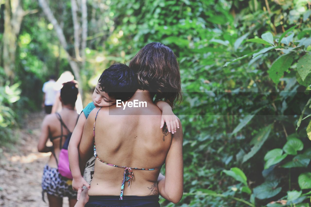 Rear view of mother carrying boy while walking in forest