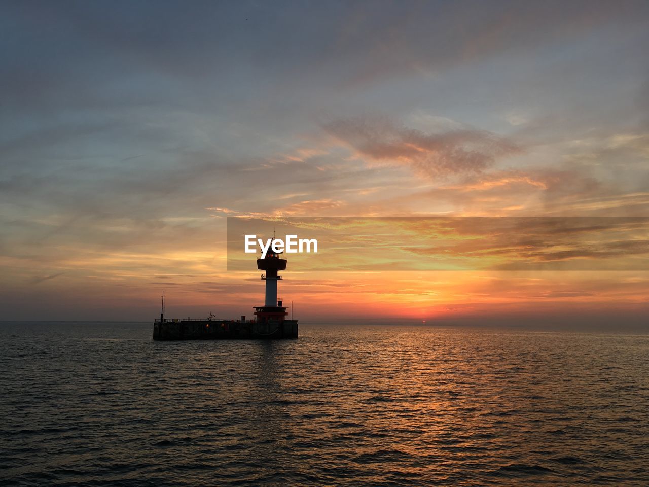 SILHOUETTE LIGHTHOUSE BY SEA AGAINST SKY AT SUNSET