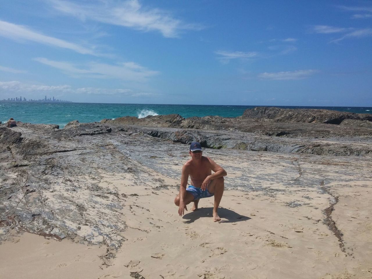 Full length of shirtless man crouching at beach against sky