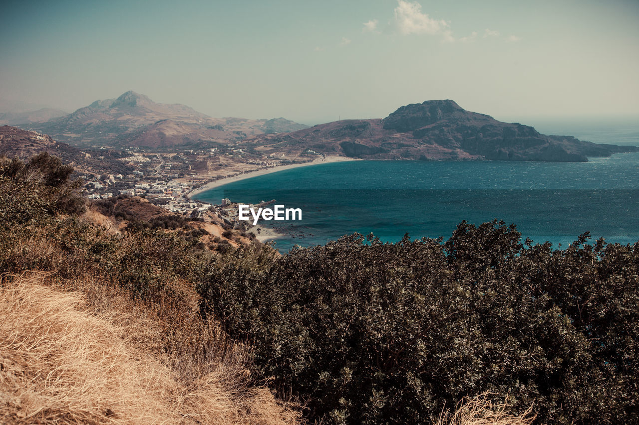 Scenic view of sea by mountain against sky