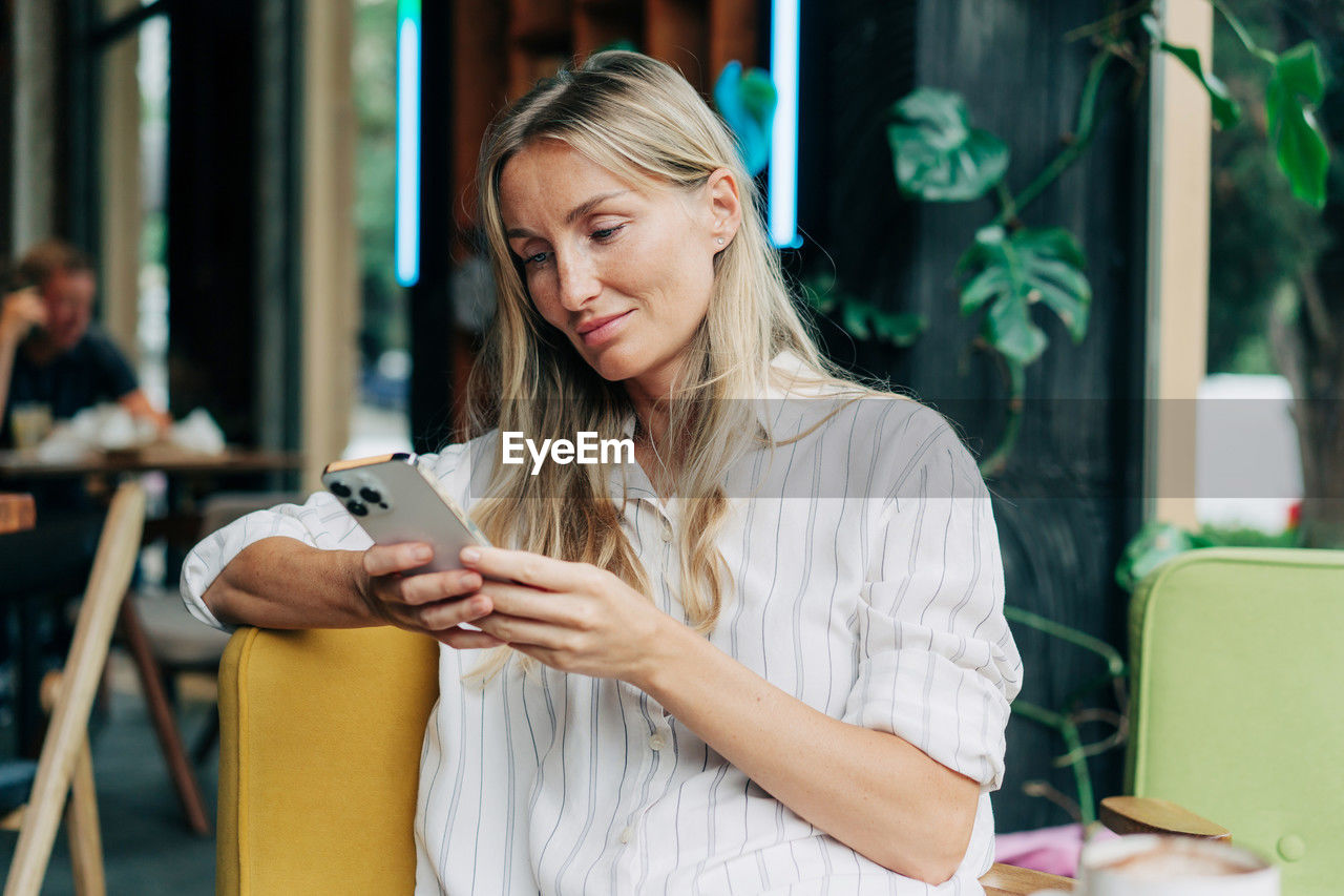 A woman uses a mobile phone to communicate while sitting in a coffee house.