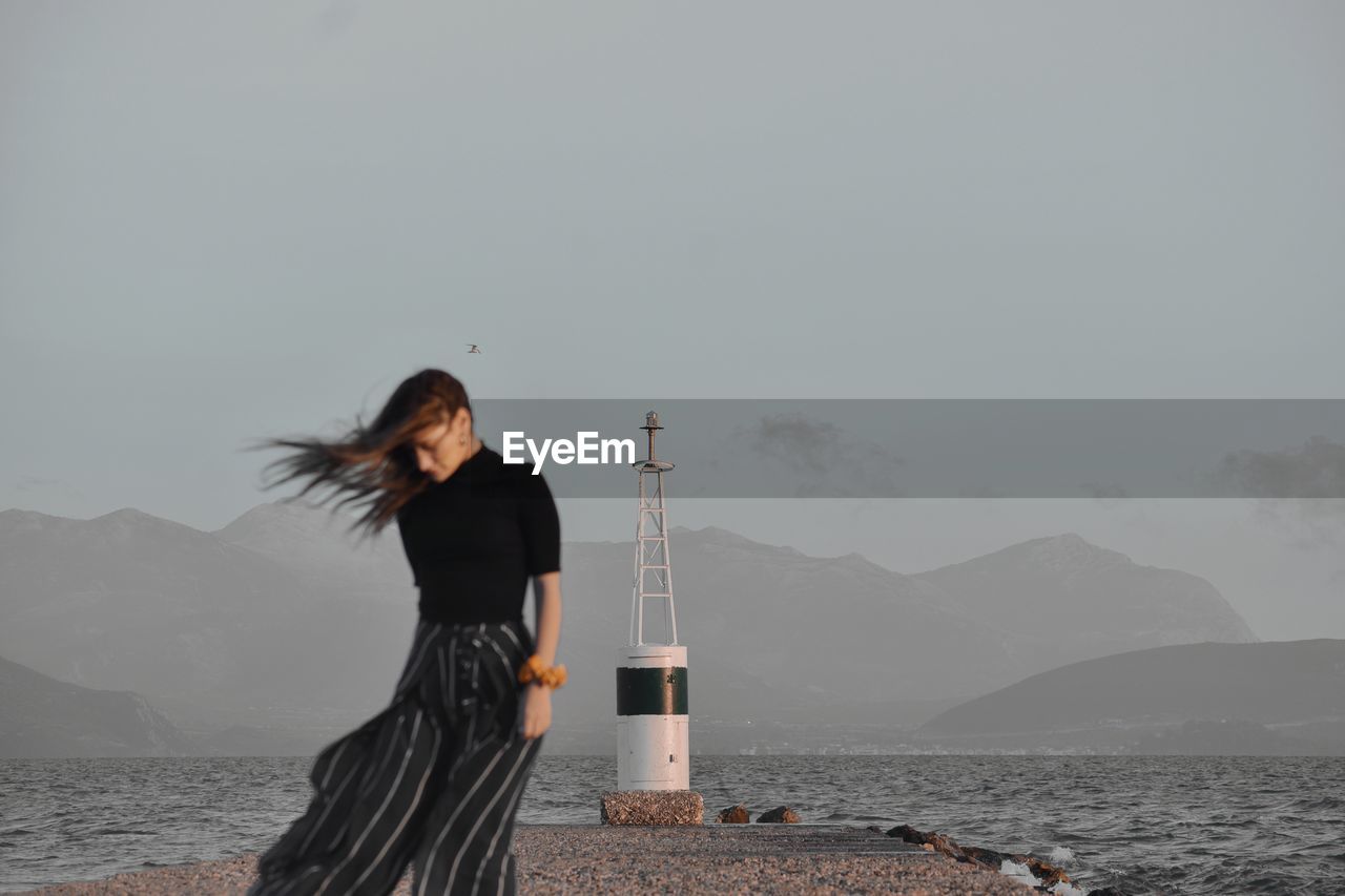 Woman standing on pier by sea against sky