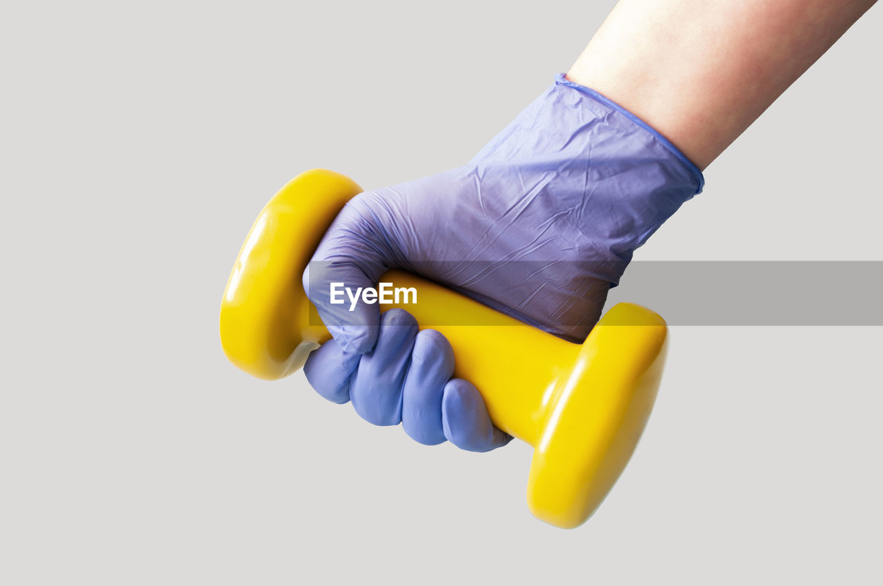 Close-up of hand holding yellow dumbbell over white background