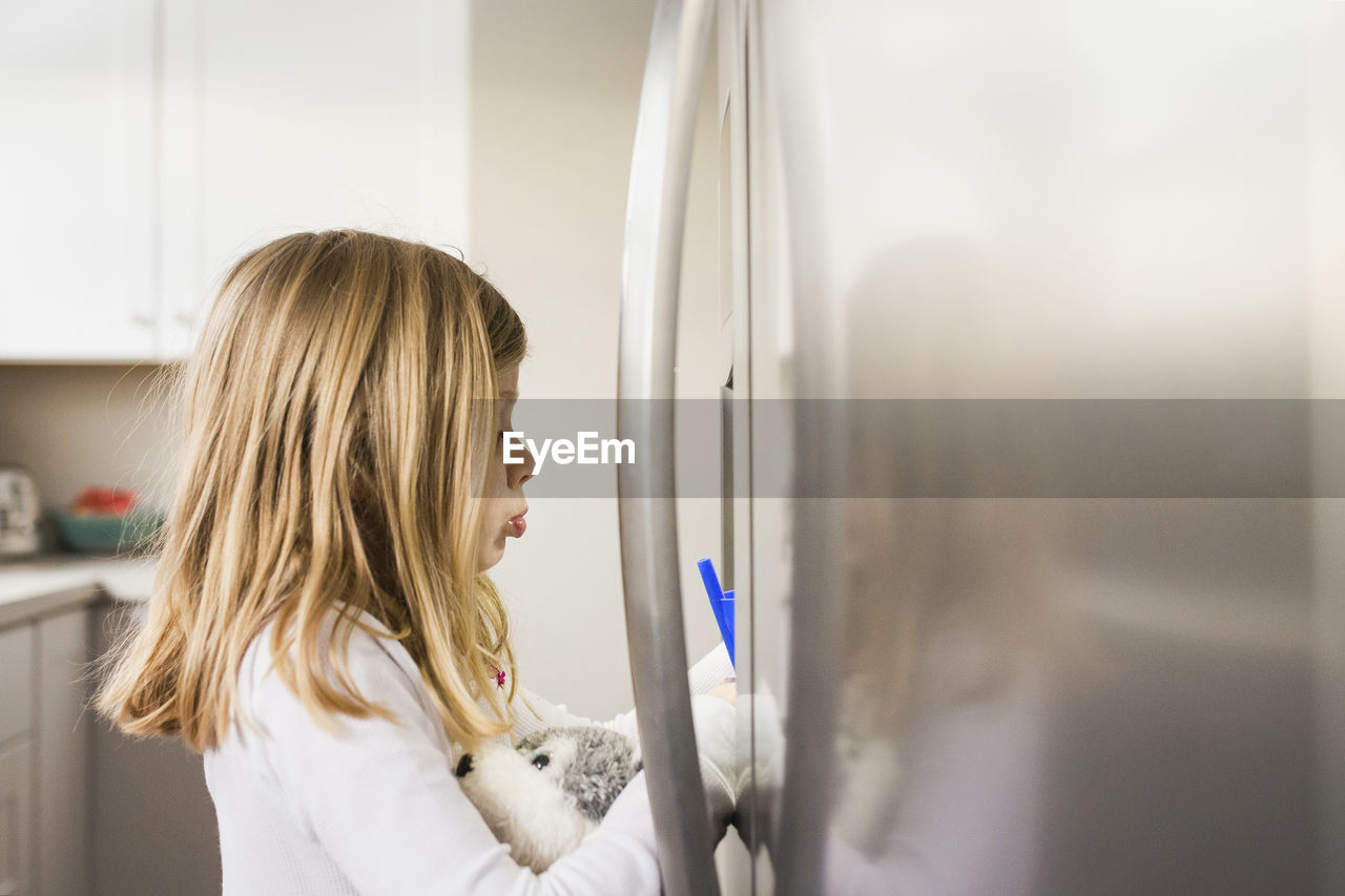 Side view of girl standing by refrigerator in kitchen at home