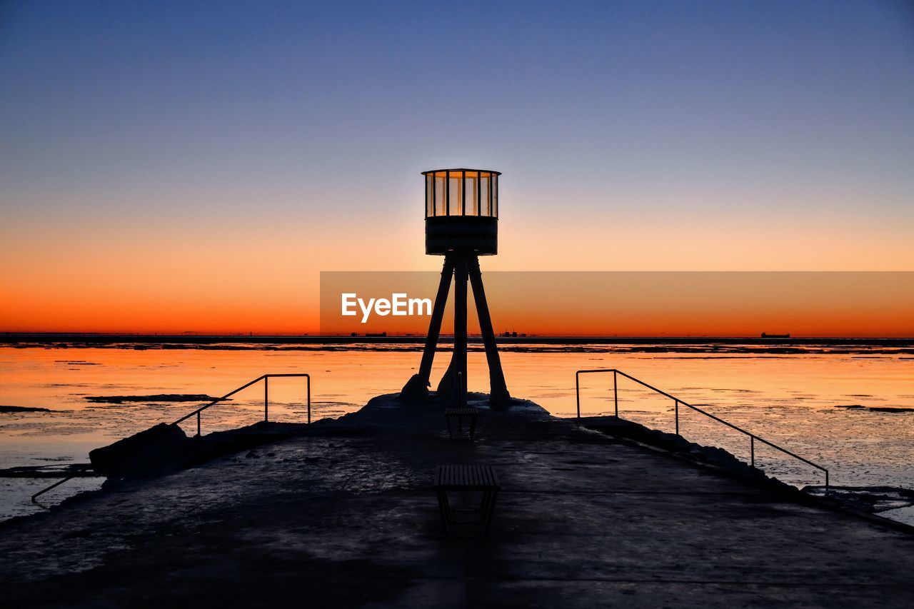 Silhouette lifeguard hut on beach against sky during sunset