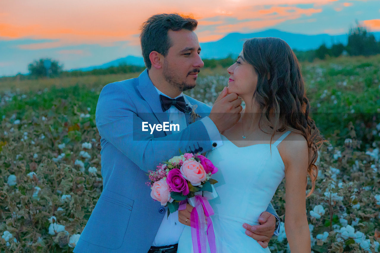 Smiling bride and groom with bouquet romancing on field