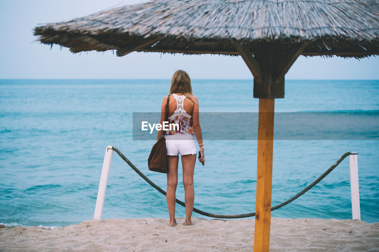 Rear view of woman standing on beach against clear sky