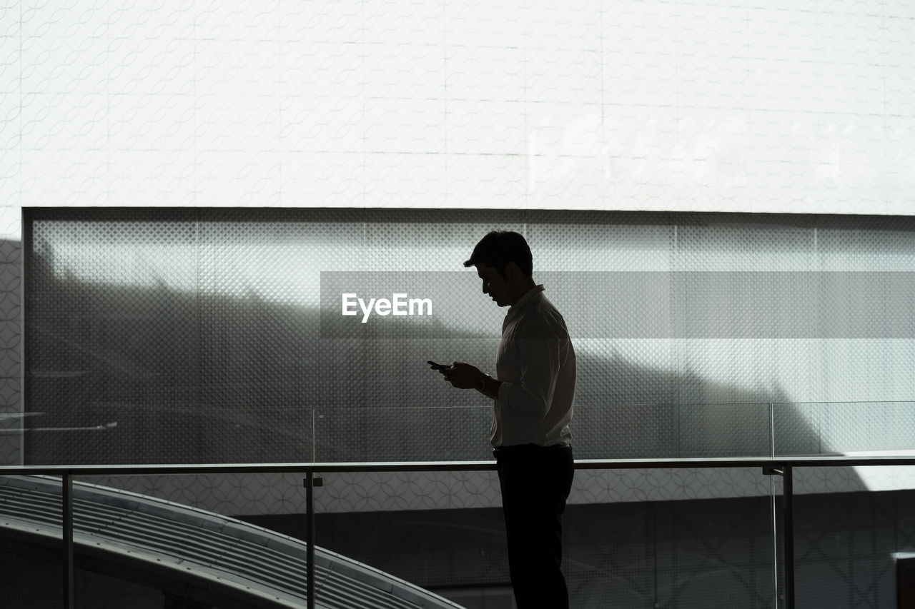 Side view of man using mobile phone against wall