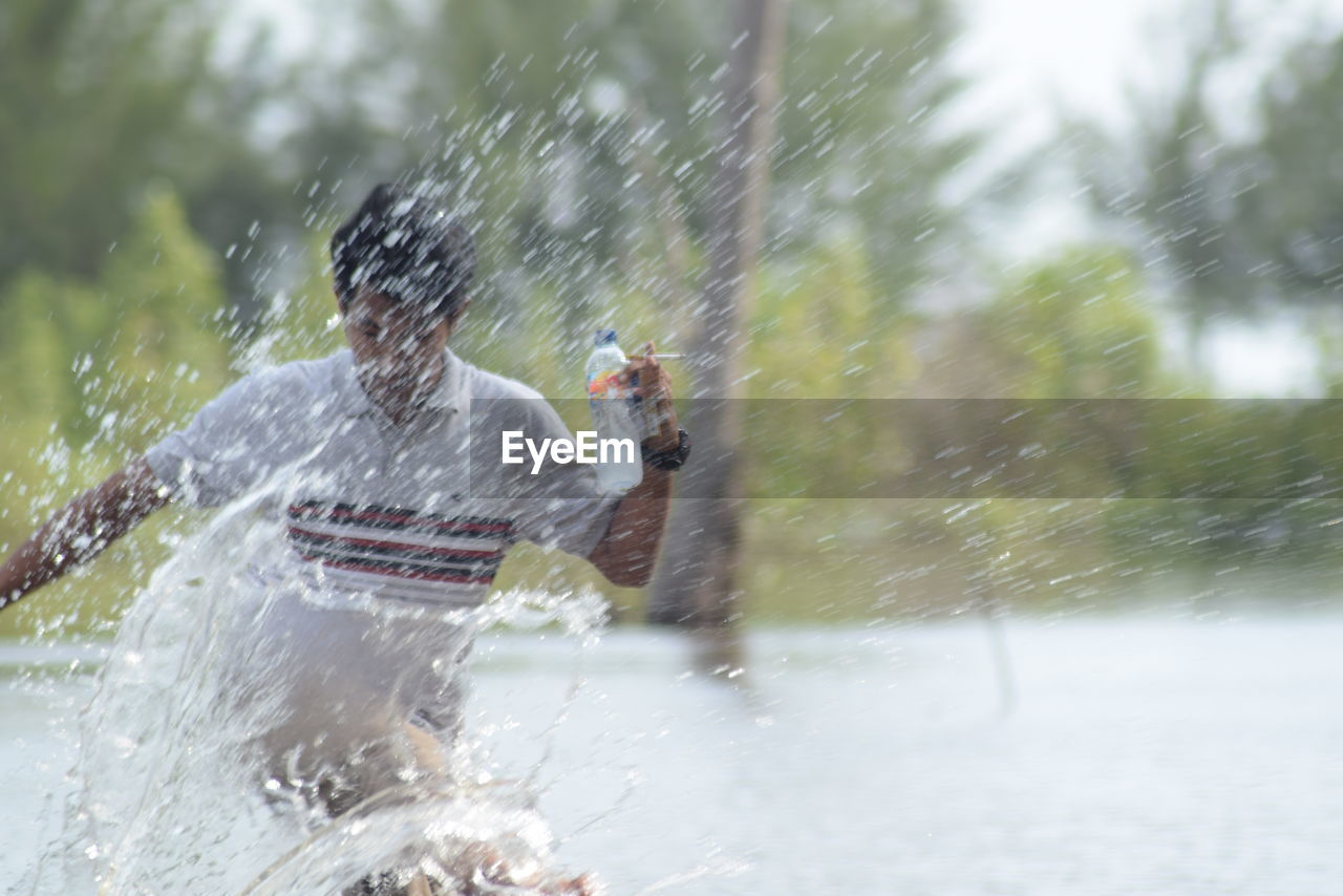 Young man splashing water while running during sunny day