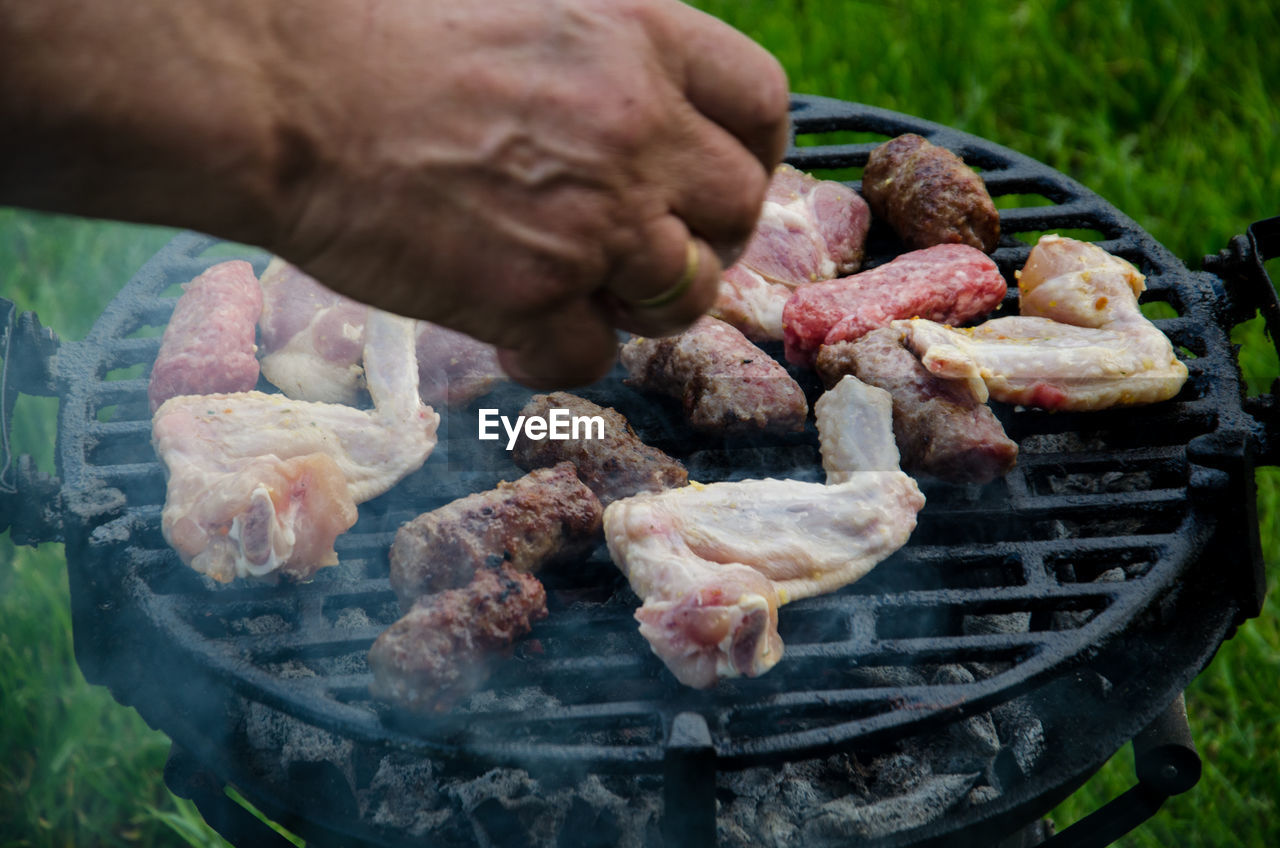 Cropped hand preparing food on barbecue grill