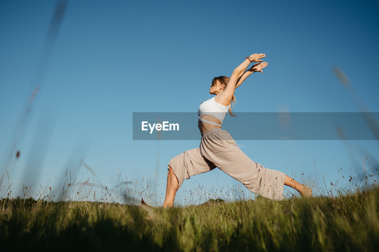 Young woman practicing yoga outdoors in the field with blue sky on the background	
