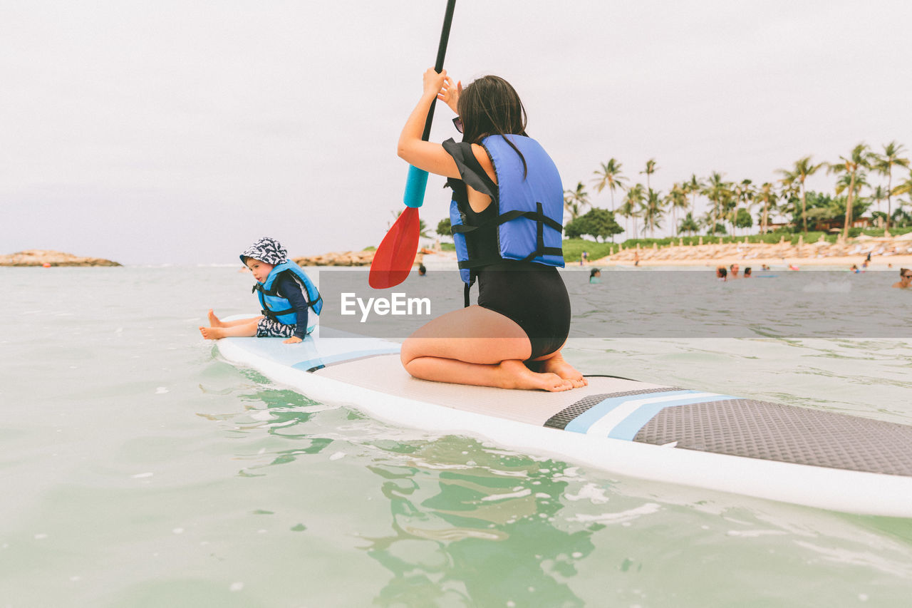 Woman with baby boy on paddleboard in sea against sky