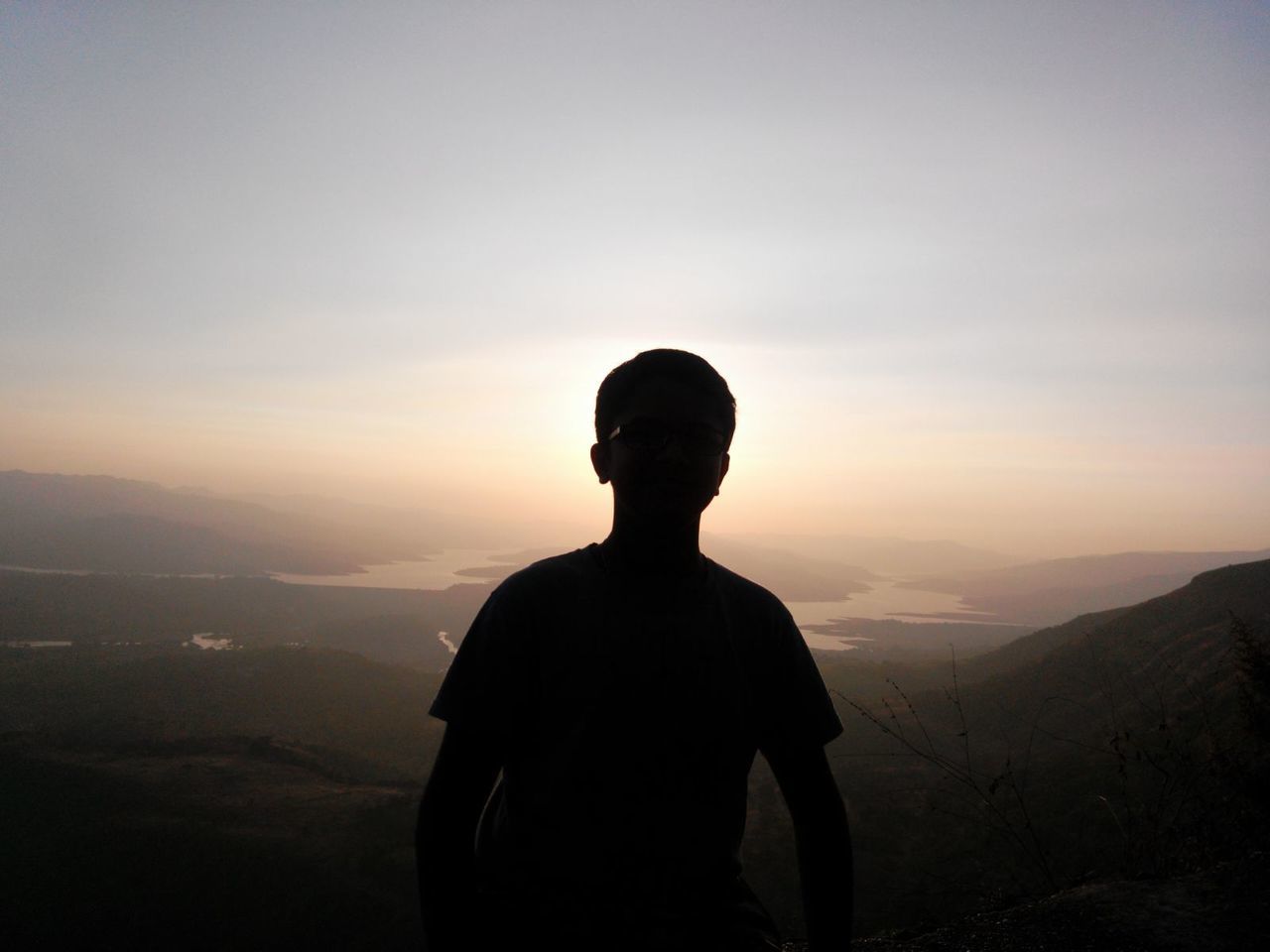 Silhouette boy standing on mountain against sky during sunset