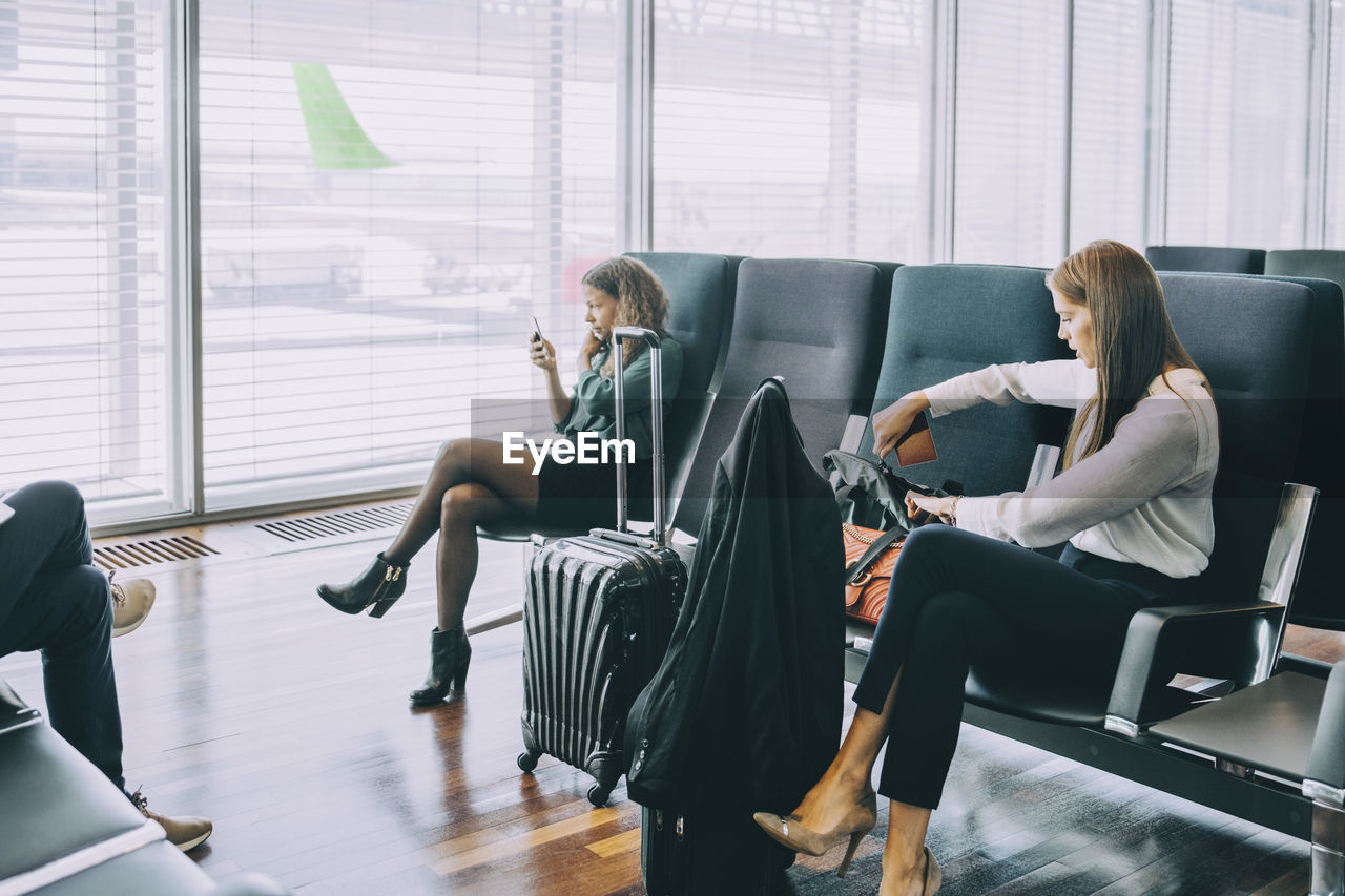 Young businesswoman removing passport from purse while sitting at airport departure area