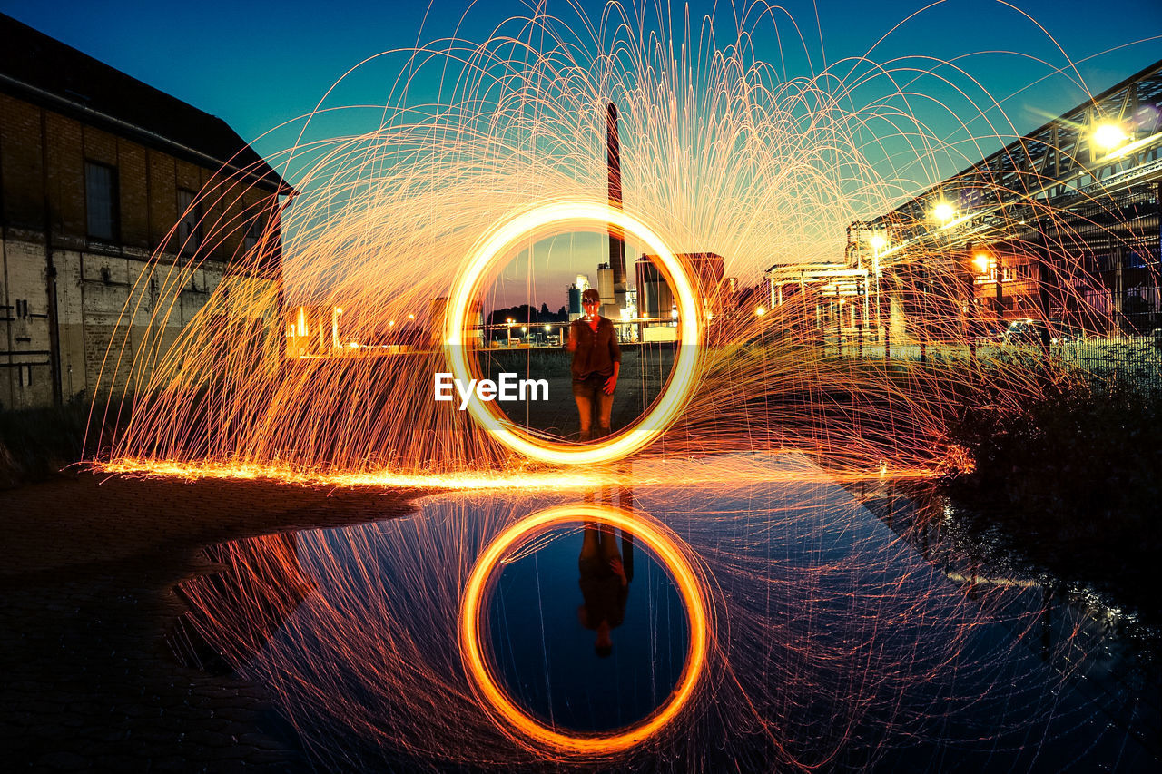 Reflection of man spinning wire wool on puddle during sunset