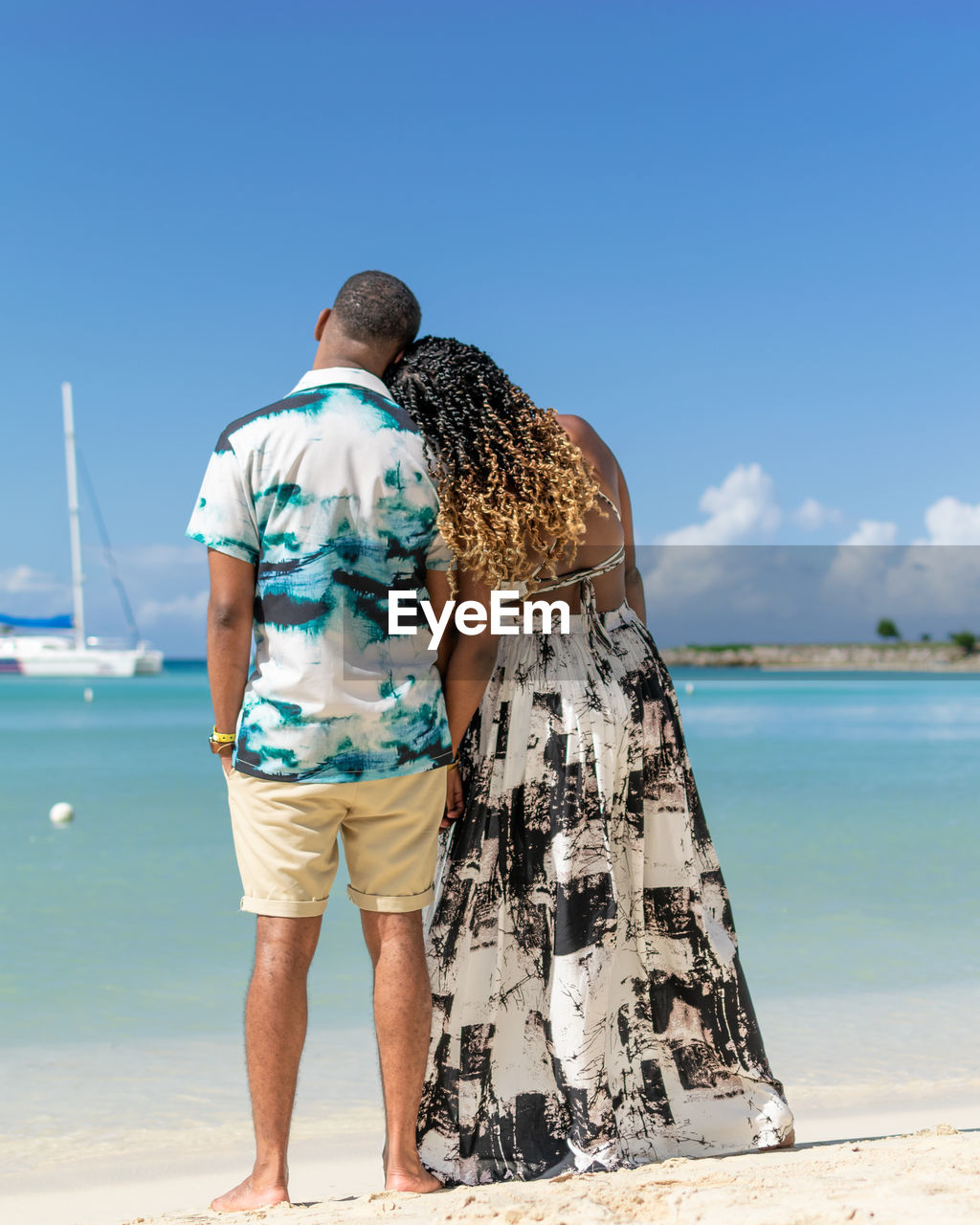 Rear view of a young couple standing at beach while looking toward the horizon