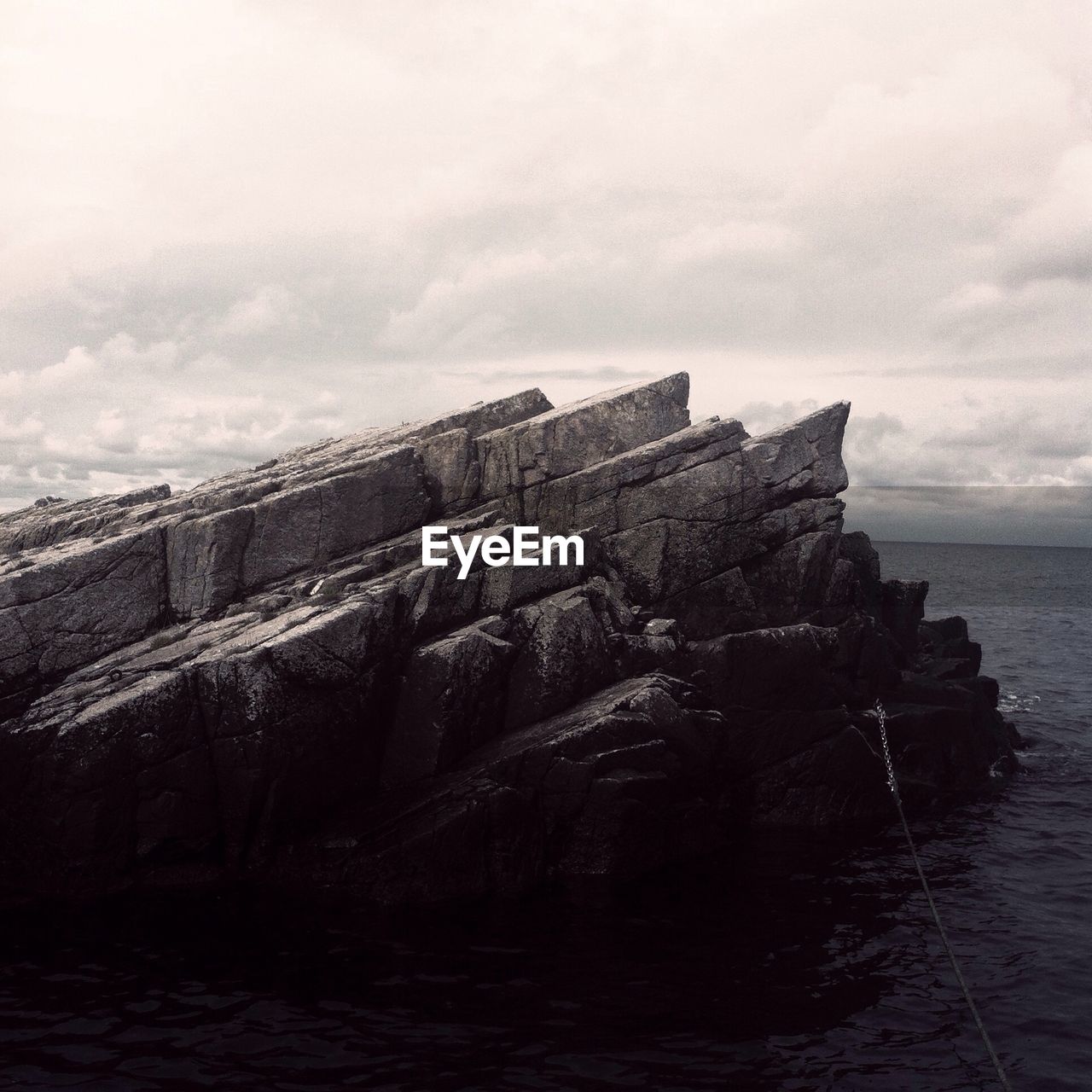 Rocks in sea against cloudy sky