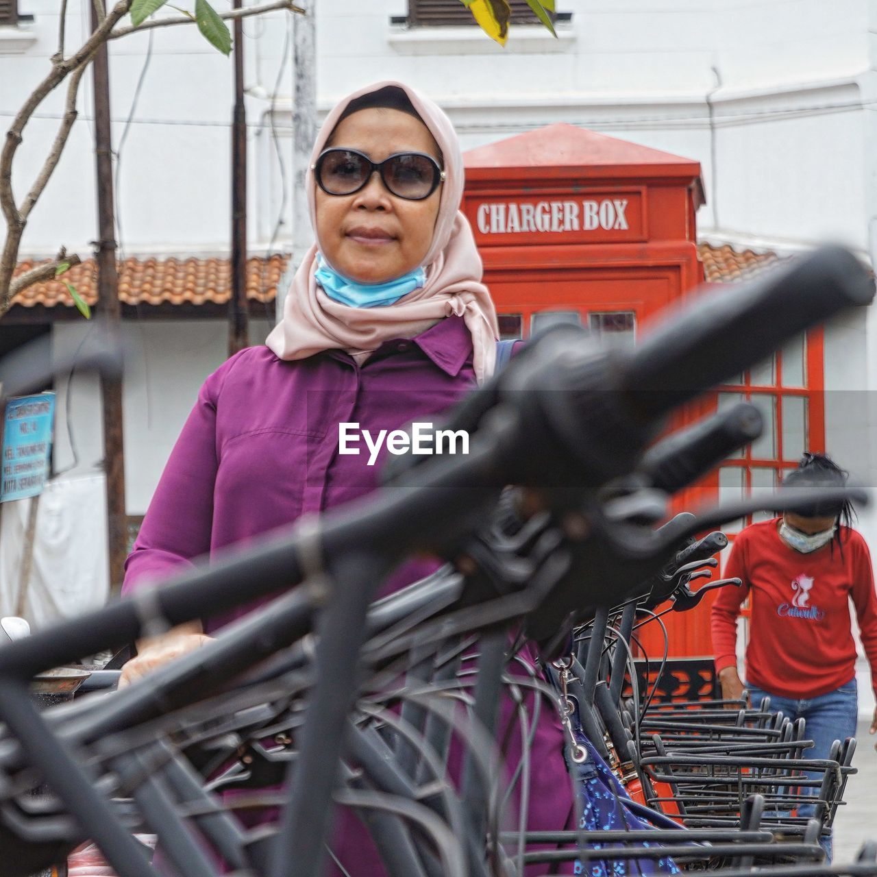 adult, one person, glasses, vehicle, women, bicycle, transportation, portrait, smiling, front view, fashion, sunglasses, clothing, day, young adult, protection, selective focus, focus on background, mode of transportation, lifestyles, sports, female, security, outdoors, eyeglasses, human face, occupation, cycling, standing, looking at camera, leisure activity, happiness, waist up, business finance and industry
