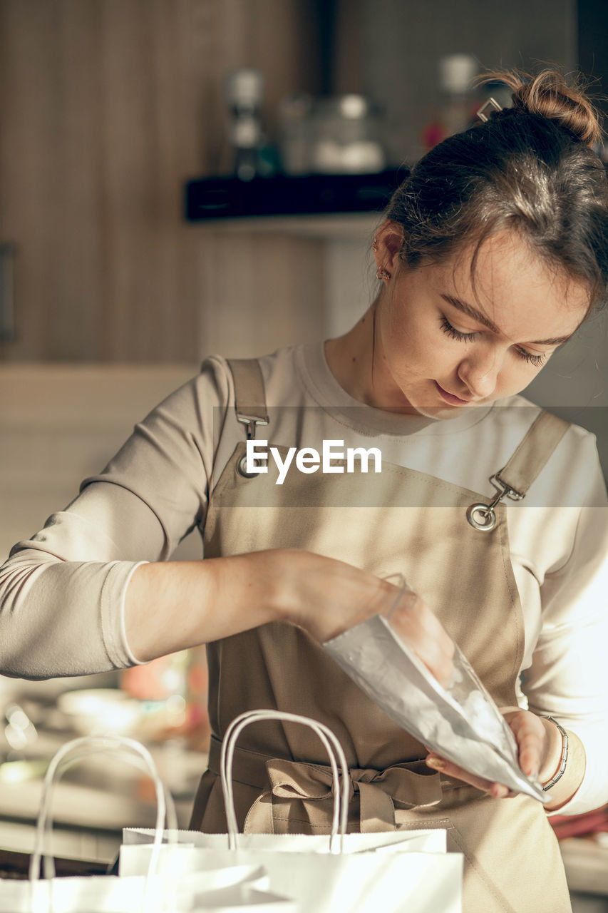 Woman bakery shop owner pours confetti into a bag for customer order. food delivery concept.