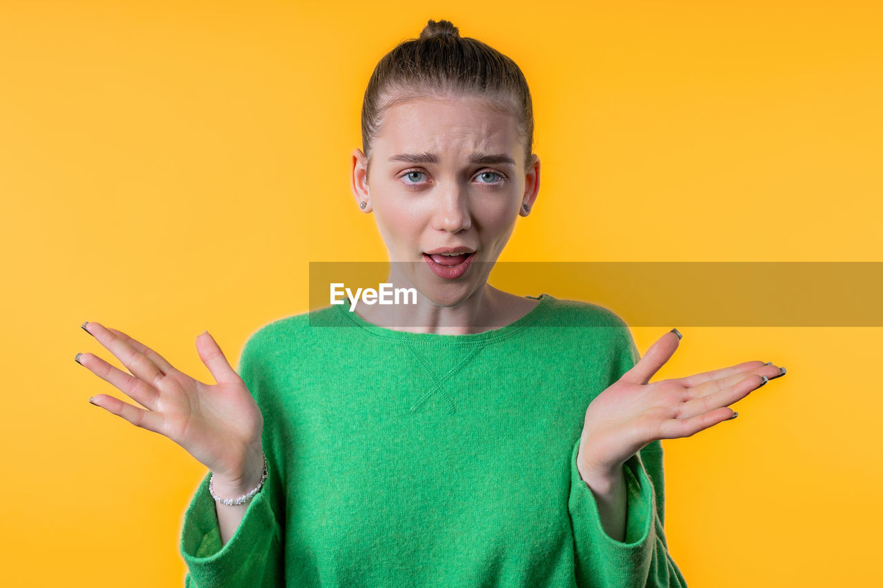 yellow, studio shot, colored background, one person, portrait, adult, emotion, indoors, women, looking at camera, yellow background, facial expression, young adult, smiling, communication, waist up, sign language, person, wireless technology, front view, green, gesturing, casual clothing, technology, hand, clothing, happiness, orange color, teenager, copy space, finger, standing, fun, human face, humor, hairstyle, holding, negative emotion, t-shirt, female