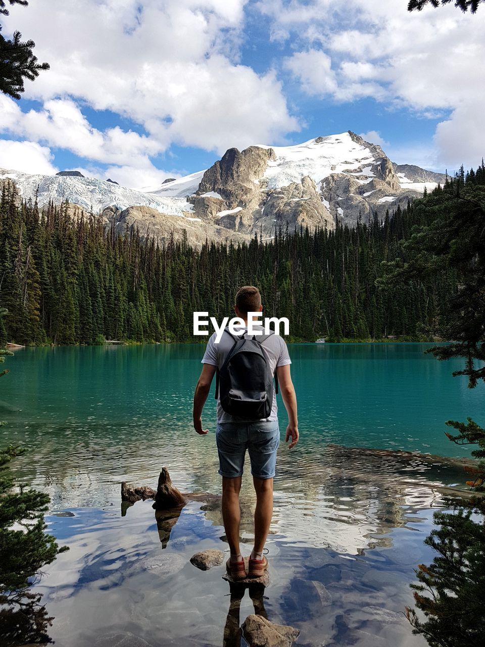 REAR VIEW OF MAN WITH DOG ON ROCK BY LAKE