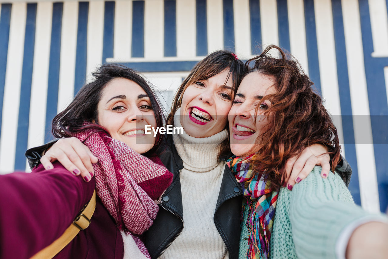 Happy women friends using mobile phone in front of colorful houses.costa nova, aveiro, portugal