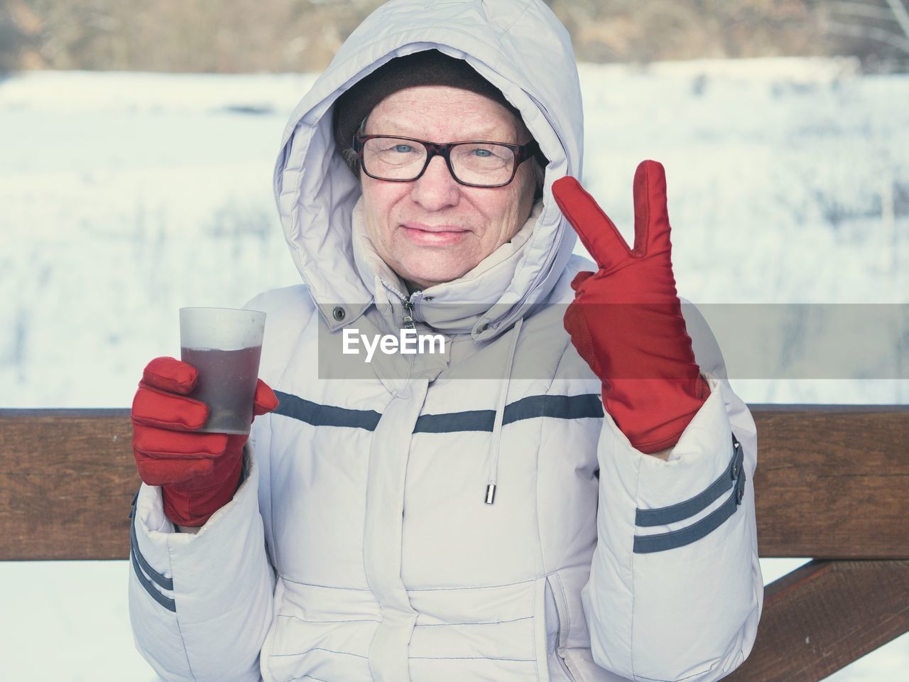 Portrait of senior woman with drink showing peace sign during winter
