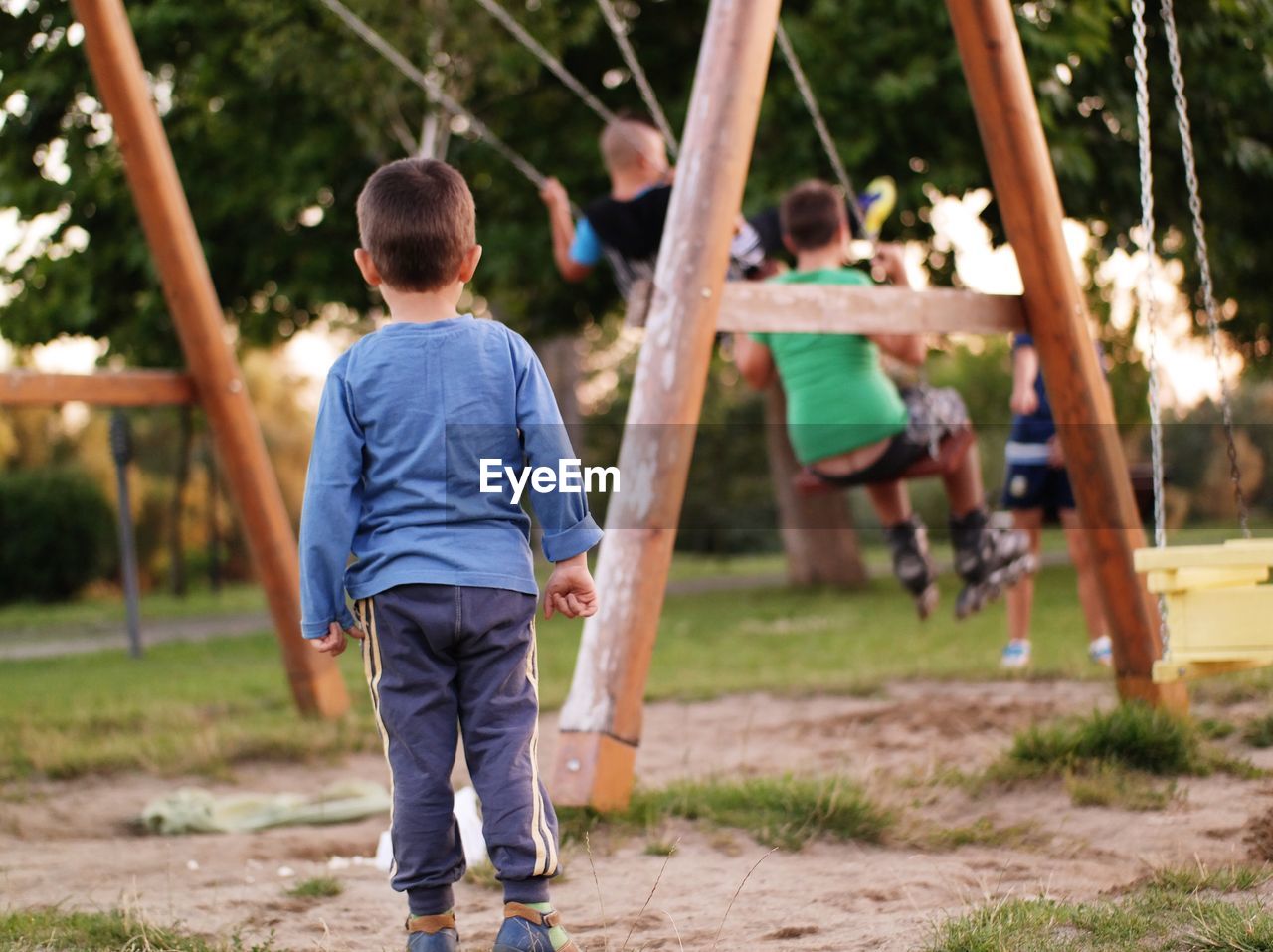 Rear view of boy standing by swing at playground