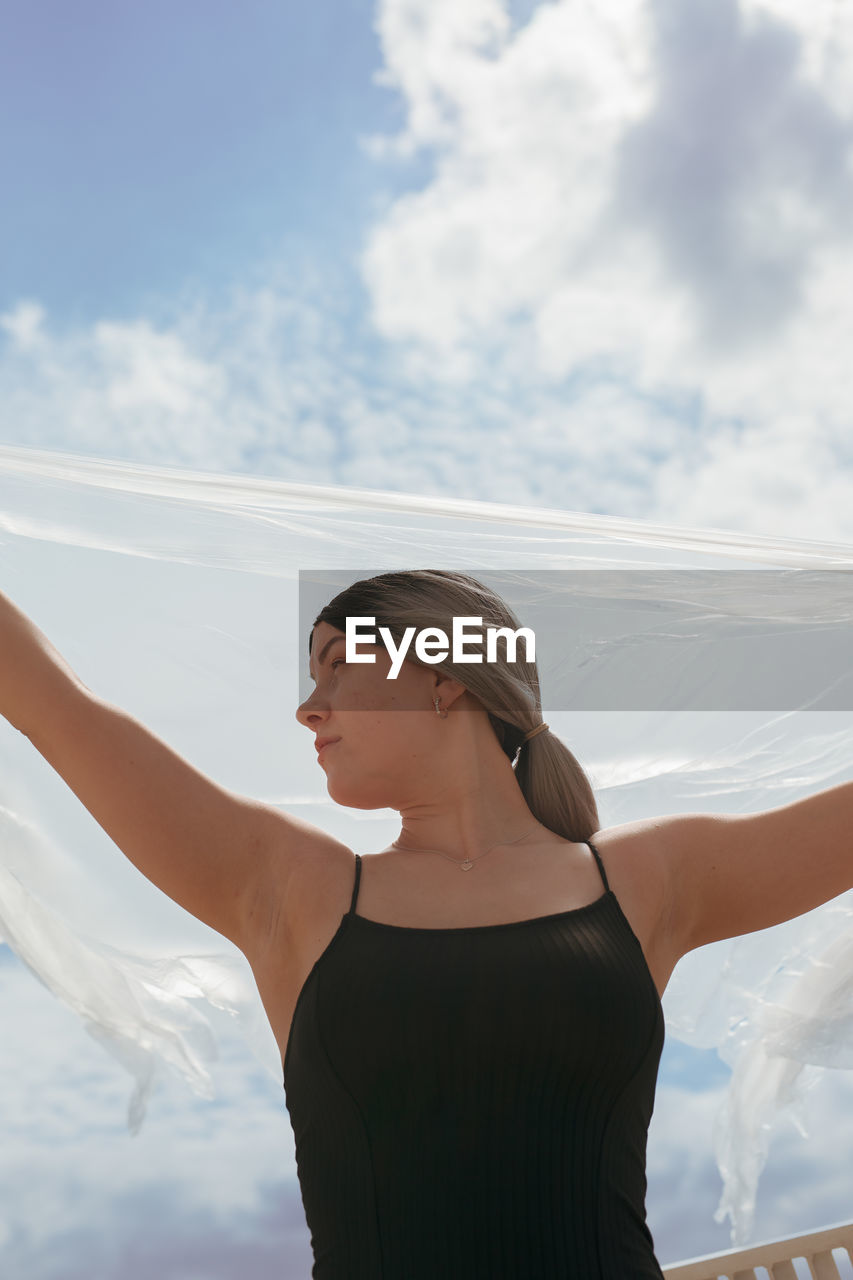 Woman standing with arms raised against sky