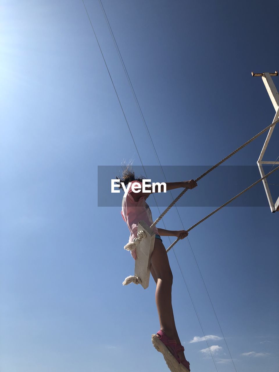 Low angle view of girl sitting on swing against blue sky