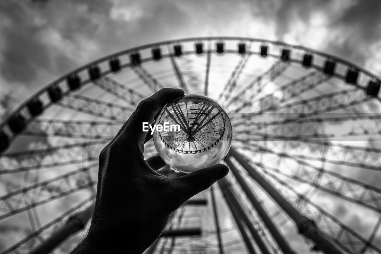 Cropped hand of person holding crystal ball with reflection of ferris wheel