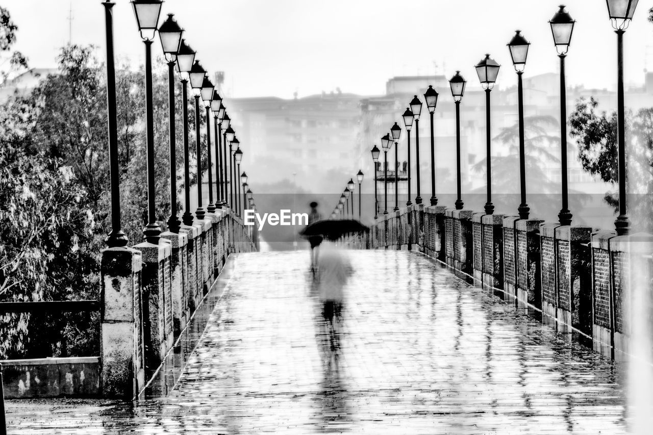 REAR VIEW OF PERSON WALKING ON FOOTBRIDGE DURING RAINY SEASON