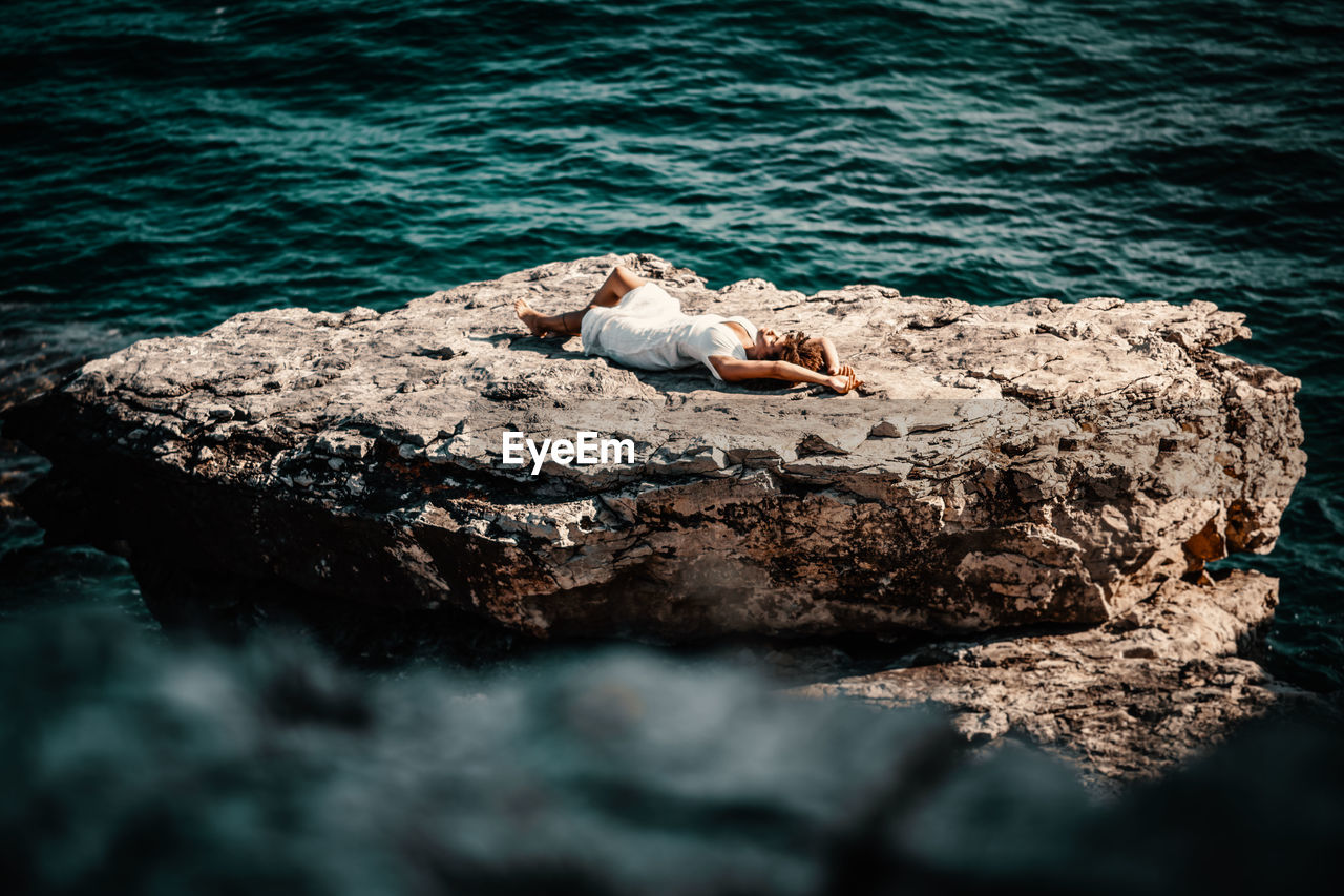 Teenage girl lying on rock in sea