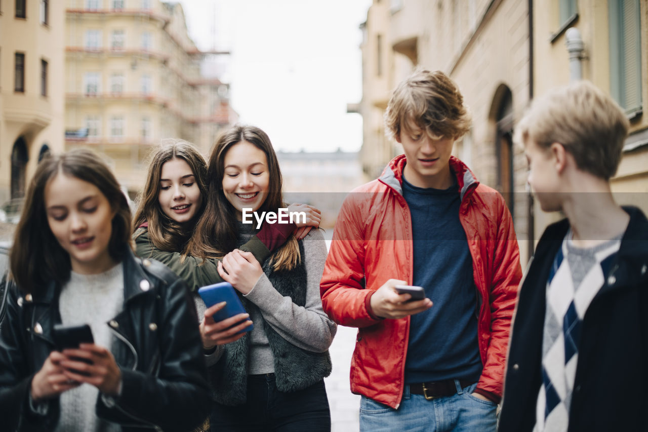 Male and female friends using smart phone in city